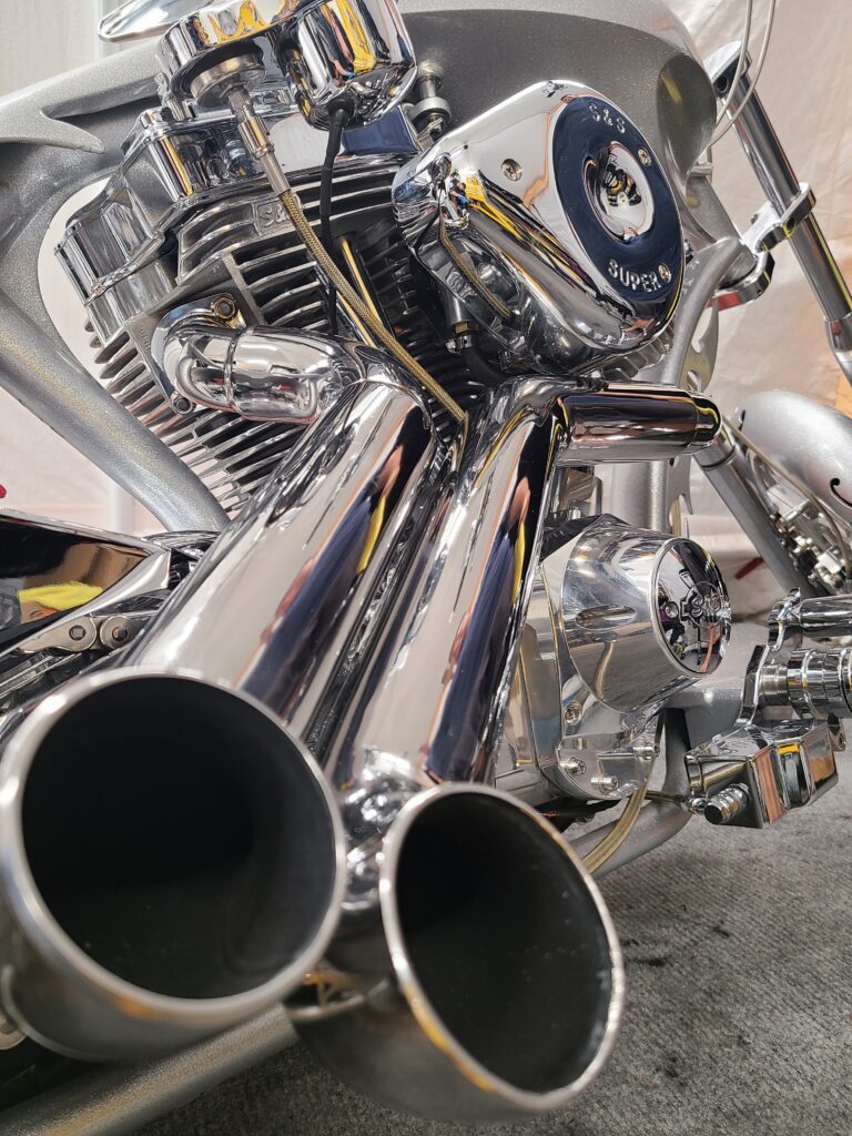 Closeup of polished chrome dual exhaust outlets and S&S engine on silver chopper
