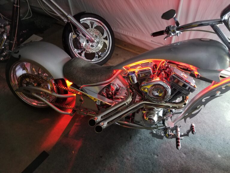 Rear side of silver custom chopper with red accent lighting and wide tire
